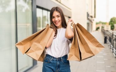 hermosa-joven-sosteniendo-bolsas-de-la-compra-y-sonriendo-al-aire-libre-scaled.jpg